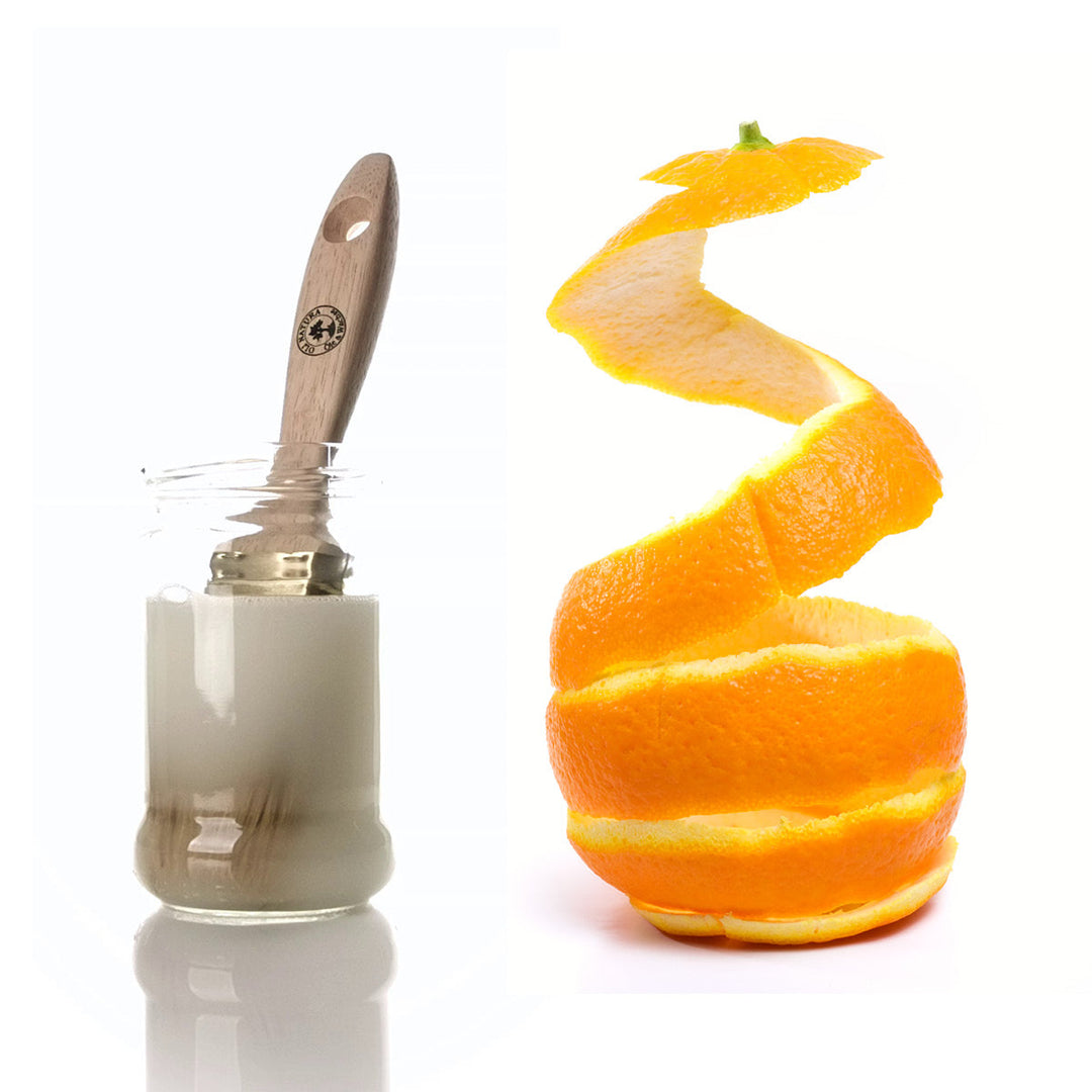 Pinsel im Reinigungsglas neben einer spiralförmigen Orangenschale